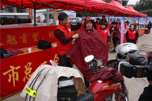梧州市總工會的黨員義工們在市東出口春運服務(wù)站助力“摩托大軍”平安返鄉(xiāng)，幫助他們檢查車輛和行李，穿上雨衣。--黃賀峰攝.j